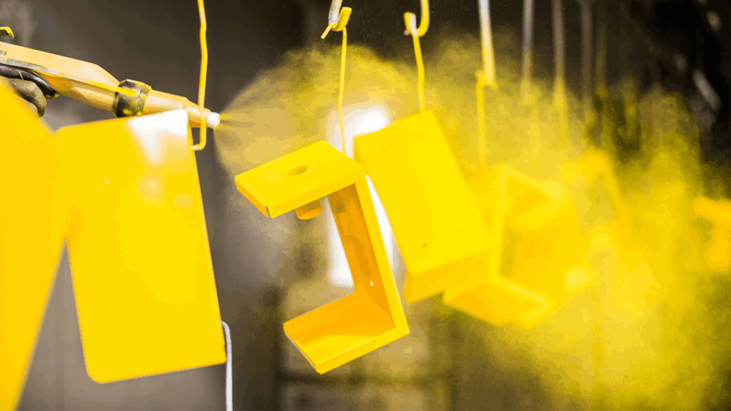 metal parts on assembly line getting sprayed by yellow powder coating